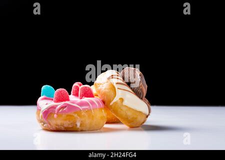 Foto einer Komposition aus 3 Donuts, die mit farbiger Schokolade, Gelee-Bohnen und Schokoladenkeksen verziert sind.das Foto wurde auf einem weißen Tisch und einem weißen Tisch aufgenommen Stockfoto