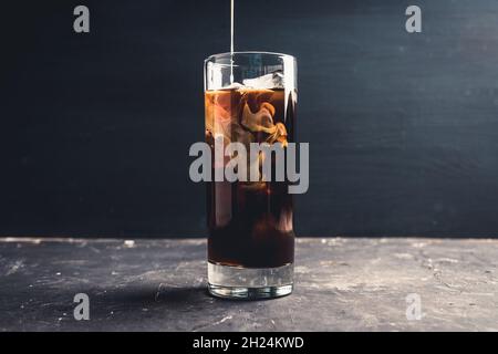 Gießen von Creme in Glas mit Kaffee. Selektiver Fokus. Stockfoto