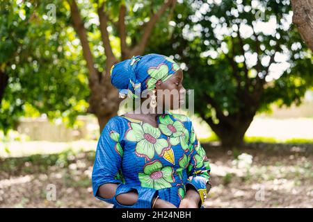 Schöne schwarze afrikanische Dorfbewohner in einem farbenfrohen traditionellen Kleid mit passender Kopfbedeckung Stockfoto