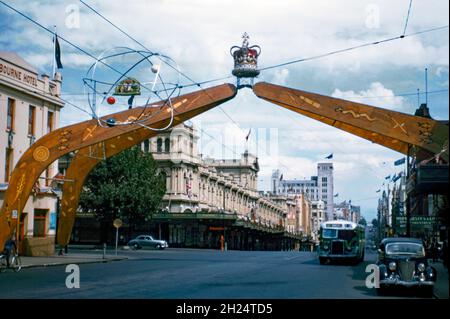 Ein Gedenkbogen in Form von vier Bumerangs in der Bourke Street, Melbourne, Victoria, Australien im Jahr 1954. Es wurde errichtet, um den königlichen Besuch von Königin Elizabeth II. Auf ihrer Krönungsreise durch das Land zu feiern. Der imposante Bogen hat ein Interessantes Design, mit indigener Aborigine-Kunst gekrönt mit der königlichen Krone (es wäre wahrscheinlich politisch nicht richtig, die beiden heute so zu mischen). Vorne ist eine ‘atomare’ Hängeskulptur/Mobile zu sehen. Der gleiche Bogen wurde erstmals in Sydney für den Besuch der Königin in dieser Stadt verwendet. Dann wurde es schnell nach Melbourne verlegt – ein altes Foto aus den 1950er Jahren. Stockfoto