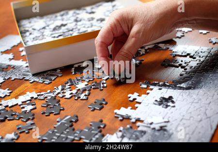 Ältere weibliche Person tut Puzzle auf Holztischplatte Stockfoto