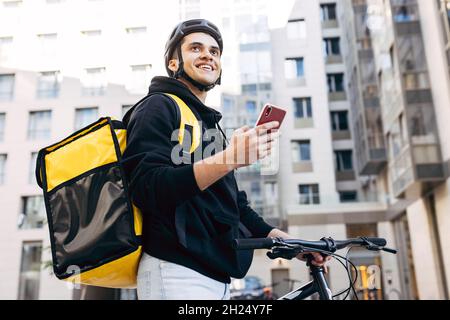 Porträt der Geburt Mann mit einem Mobiltelefon, trägt thermische Rucksack stehen gegen Wohngebäude Stockfoto