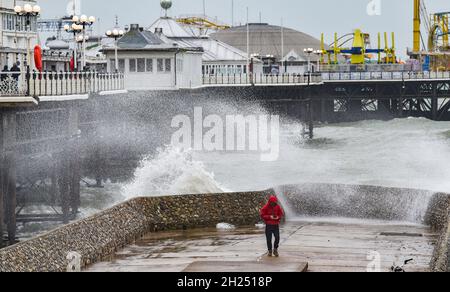 Brighton UK 20. Oktober 2021 - Ein Spaziergänger wird von Wellen durchnässt, die an der Strandpromenade von Brighton am Pier einstürzen, während heute Regen und starke Winde über Großbritannien hinwegfegen. : Credit Simon Dack / Alamy Live News Stockfoto