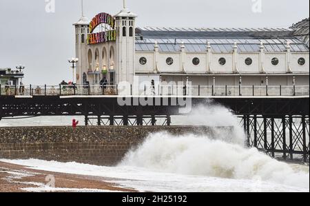 Brighton UK 20. Oktober 2021 - die Besucher werden von den Wellen durchnässt, die an der Strandpromenade von Brighton am Palace Pier einstürzen, während heute Regen und starke Winde über Großbritannien ziehen. : Credit Simon Dack / Alamy Live News Stockfoto