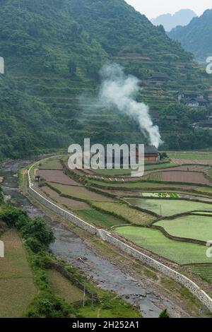 Rauch steigt aus einem Bauernhaus, das von terrassenförmigen Reisfeldern in der ländlichen Provinz Hunan, China, umgeben ist. Stockfoto