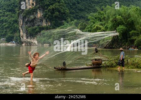 Ein Kormoran-Fischer in einem konischen Hut wirft ein Wurfnetz in den Fluss Li, Xingping, China. Stockfoto