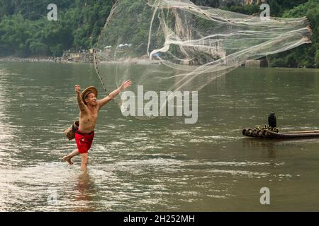 Ein Kormoran-Fischer in einem konischen Hut wirft ein Wurfnetz in den Fluss Li, Xingping, China. Stockfoto