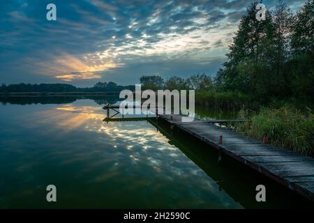 Pier über dem See und der Sonnenuntergang hinter den Wolken, Stankow, Lubelskie, Polen Stockfoto