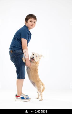 Der Hund steht auf seinen Hinterbeinen und der Junge hält ihn an seinen Vorderpfoten und beide blicken in die Kamera. Stockfoto