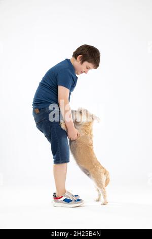 Der Hund steht auf seinen Hinterbeinen und der Junge hält ihn an seinen Vorderpfoten und sie blicken einander in die Augen. Stockfoto