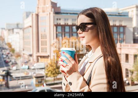 Schöne Frau mit Sonnenbrille, die im Stadtzentrum Kaffee trinkt Stockfoto