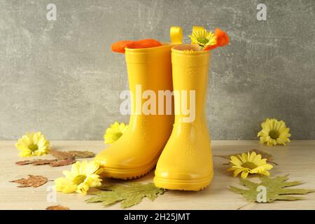 Gummistiefel mit Blumen auf Holztisch mit Blättern. Stockfoto