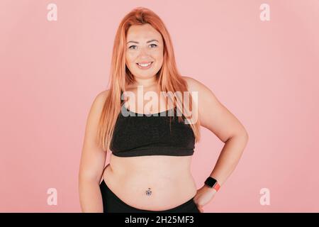 Porträt einer schönen Plus-Größe Frau trägt Sport-Outfit auf rosa Hintergrund lächelnd Blick auf die Kamera stehen. Stockfoto