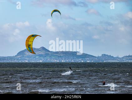 Longniddry Bents. East Lothian, Schottland, Großbritannien, 20. Oktober 2021. UK Wetter: Windiger Tag für Kitesurfer. Kitesurfer genießen an einem sonnigen Tag im Firth of Forth das stürzende Wetter mit Blick auf Edinburgh und Arthur's Seat in der Ferne über die Bucht Stockfoto