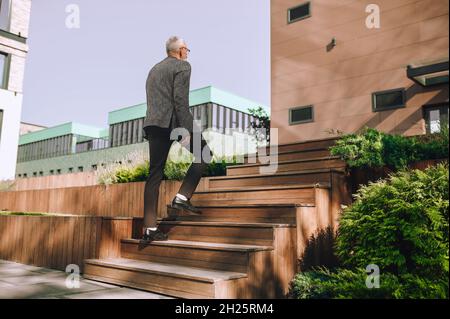 Stilvoller Geschäftsmann, der die Holztreppe im Freien aufsteigt Stockfoto