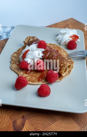 Helsinki / Finnland - 20. OKTOBER 2021: Traditionelle finnische Küche: Finnische Pfannkuchen auf einem Teller mit Schlagsahne und Himbeermarmelade auf der Seite Stockfoto