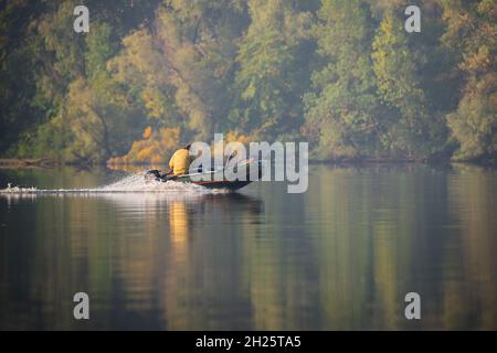 Grünes aufblasbares Gummimotorboot, das auf dem Fluss schwimmt, um auf dem Hintergrund herbstlicher Bäume zu fischen Stockfoto