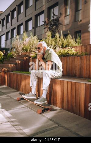 Männlicher Skateboarder mit seinen Füßen auf dem Skateboard draußen sitzen Stockfoto