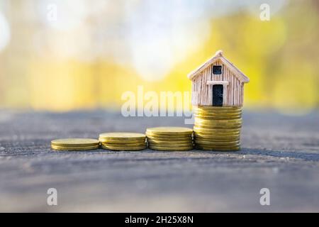 Münzen stapeln sich mit einem winzigen Spielzeughaus auf der Oberseite. Dream Home Investment und Hypothek Konzept. Stockfoto