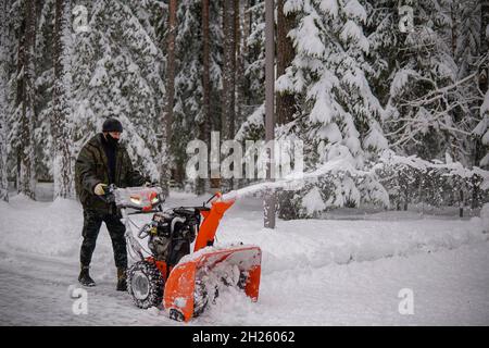 Ein Mann entfernt Schnee mit einem Schneefräsen auf dem Hintergrund eines verschneiten Waldes Stockfoto