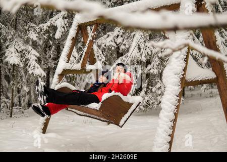 Mutter und Tochter sitzen auf einer Schaukel in einem verschneiten Wald. Stockfoto