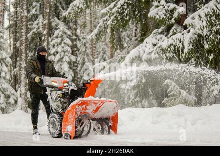 Ein Mann entfernt Schnee mit einem Schneefräsen auf dem Hintergrund eines verschneiten Waldes Stockfoto