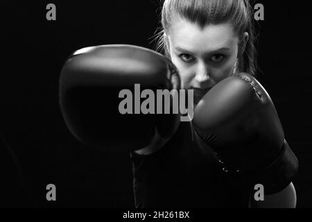 Wütend Muay Thai Boxerin in Angriff Pose. Fitness junge Frau Boxtraining auf schwarzem Hintergrund, Nahaufnahme monochrom Stockfoto