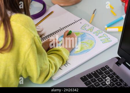 Kindermädchen zeichnet Planeten Erde mit Wachsfarben auf Schulnotizbuch für den Erdtag - kleine Aktivistin schreibt die Botschaft Save the Planet - Kindheit, prote Stockfoto