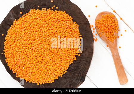 Rote Linsen und Bulgur auf einem dunklen Holzteller und ein Holzlöffel auf einem weißen Holztisch mit Kopierfläche Stockfoto