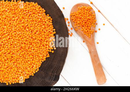 Rote Linsen und Bulgur auf einem dunklen Holzteller und ein Holzlöffel auf einem weißen Holztisch mit Kopierfläche Stockfoto