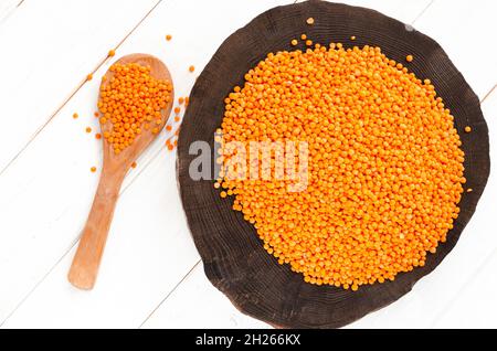 Rote Linsen und Bulgur auf einem dunklen Holzteller und ein Holzlöffel auf einem weißen Holztisch mit Kopierfläche Stockfoto