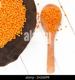 Rote Linsen und Bulgur auf einem dunklen Holzteller und ein Holzlöffel auf einem weißen Holztisch mit Kopierfläche Stockfoto