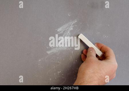 Die Hand eines erwachsenen Mannes schreibt in weißer Kreide die Zahl 1 auf einen grauen Hintergrund. Der Mann hält ein Stück weiße Kreide in der Hand. Selektiver Fokus. Stockfoto