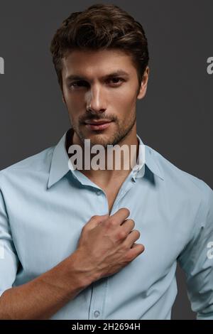 Porträt eines jungen, schönen, selbstbewussten europäischen Geschäftsmannes. Bärtiger Mann mit dunklem Haar trägt ein blaues Hemd und schaut auf die Kamera. Isoliert auf dunkelgrauer BA Stockfoto