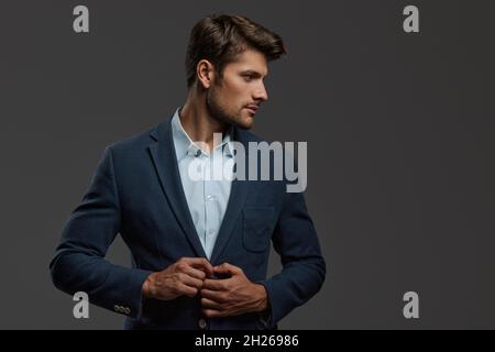 Profil eines jungen, wunderschön fokussierten europäischen Geschäftsmannes. Vorderansicht eines bärtigen Mannes mit dunklem Haar, der eine Business-Jacke trägt und die Kamera anschaut. Isola Stockfoto