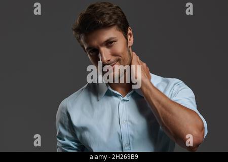 Junger, schön lächelnder europäischer Geschäftsmann. Bärtiger Mann mit dunklem Haar trägt ein blaues Hemd und schaut auf die Kamera. Isoliert auf dunkelgrauem Hintergrund. Nieten Stockfoto