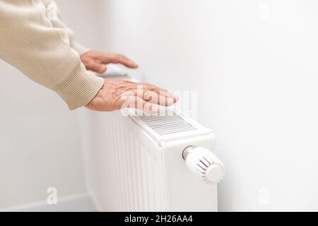 Ein älterer Mann wärmt seine Hände über einem elektrischen Heizgerät. In der Nebensaison wird die Zentralheizung verzögert, sodass die Leute zusätzliche Heizungen kaufen müssen Stockfoto