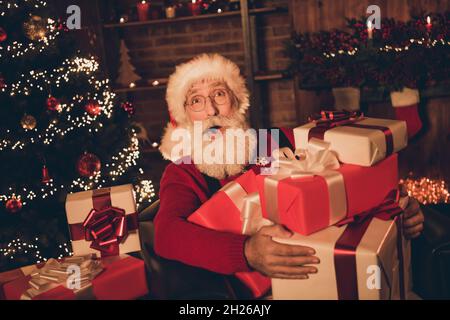 Foto von lustig beeindruckt reifen Mann gekleidet santa Kostüm hält viele Geschenk-Boxen im Haus Zimmer Stockfoto