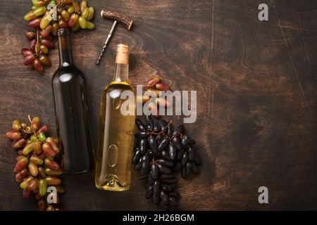Weinflaschen mit Weintrauben und Weinläsern auf altem dunklen Holztischhintergrund mit Kopierraum. Rotwein mit Weinrebe. Weinkomposition auf rustikal Stockfoto