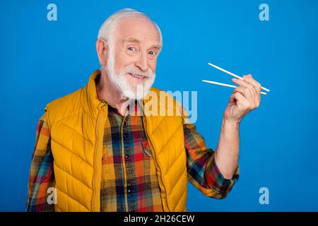 Porträt eines attraktiven, fröhlichen, grauhaarigen Mannes, der östliche Nahrung mit Stöcken isst, die auf einem hellblauen Hintergrund isoliert sind Stockfoto