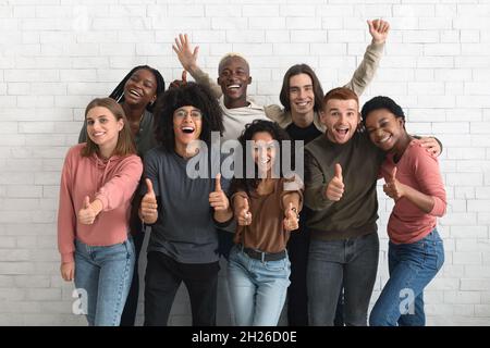 Schöne, multiethnische junge Menschen, die über einer weißen Ziegelmauer posieren Stockfoto