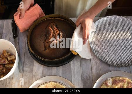 Schritt-für-Schritt-Prozess der Herstellung einer sauren Creme Schokolade Kuchen. Frauenhände nehmen den fertigen Kuchen aus dem Ofen und legen ihn auf eine Schüssel. Backconcep Stockfoto