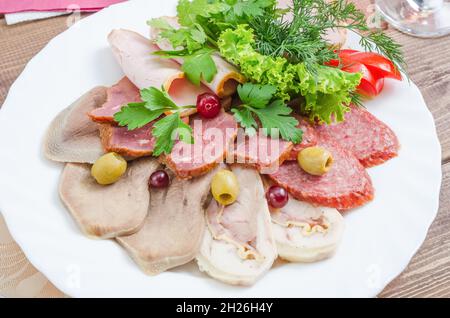 Aufschnitt: Zunge, geräucherte Wurst, Schinken, der mit Kräutern auf einem weißen Teller aus nächster Nähe garniert ist Stockfoto