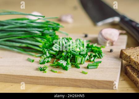 Grüne Zwiebeln auf einem Holzbrett verchromt, Knoblauch, Brot, Pfeffer und Messer Stockfoto