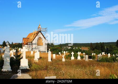 Eine alte Kirche, die repariert wird, mit Gerüsten, die um sie herum auf einem alten, überwucherten Friedhof errichtet wurden. Stockfoto