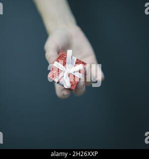 In den Fingern der Frauen liegt eine kleine rote Schachtel mit einem weißen Bogen Stockfoto