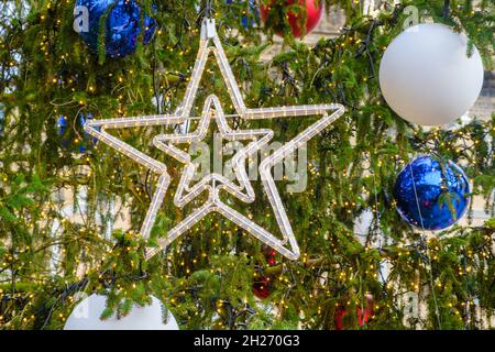 Großer Stern und Spielzeugkugeln auf dem Weihnachtsbaum auf der Straße. Vorbereitung auf die Weihnachtsferien. Stockfoto