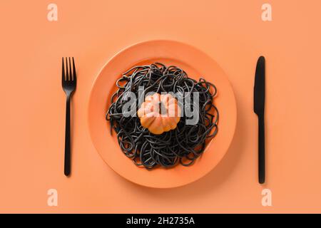 Halloween kreative italienische schwarze Pasta Tintenfisch Tinte verziert Kürbis in orange Platte auf weißem Hintergrund. Blick von oben. Lebensmittelkonzept. Lustige Tischset Stockfoto