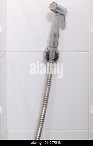 Das moderne Bidet-Spray hängt an der weißen Fliesenwand in der Toilette des Stadthauses, sauber und hygienisch für den Benutzer, Vorderansicht für die Kopie s Stockfoto