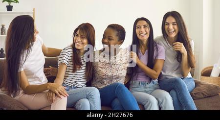 Eine vielfältige Gruppe von glücklichen jungen Frauen, die auf der Couch sitzen, miteinander reden und Spaß haben Stockfoto